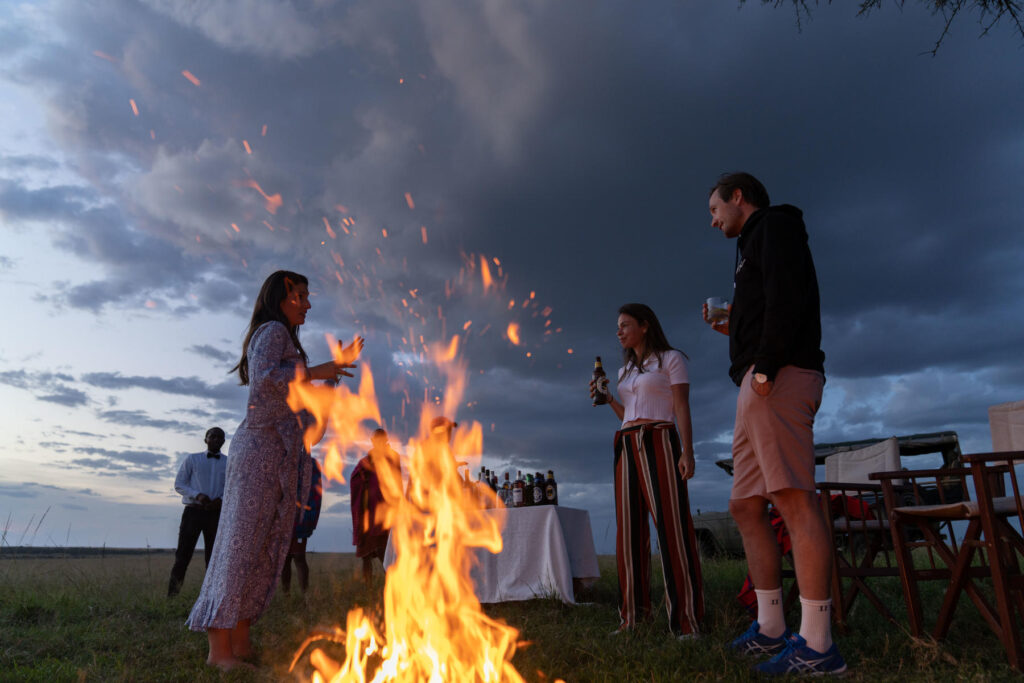 Group of people standing around a fire as it starts to become night | Photo credit: Basecamp Adventure